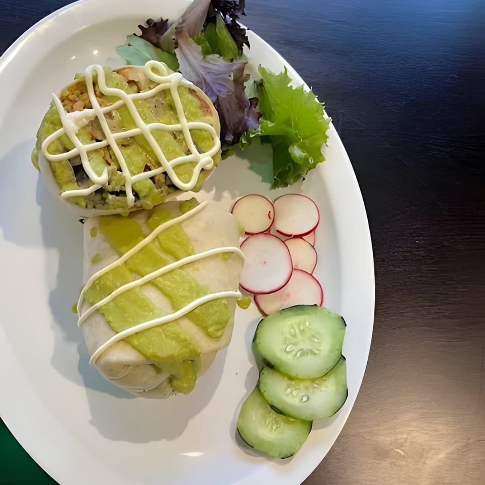 Two burritos drizzled with green sauce and white crema, served with a side salad, radishes, and cucumbers.