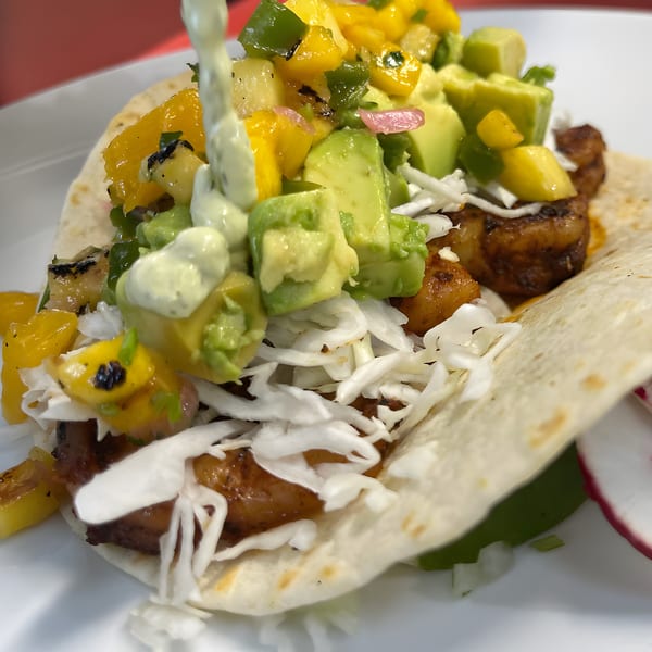 A Silantro Lime Tacos shrimp taco with mango salsa, avocado, and creamy sauce being drizzled.