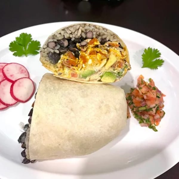 A cut burrito revealing rice, black beans, avocado, and scrambled eggs, served with salsa and radishes.