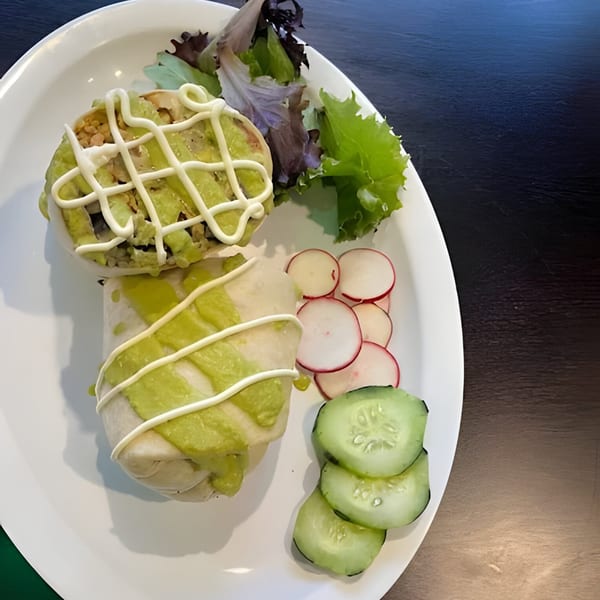 Two burritos drizzled with green and white sauce, served with salad, radishes, and cucumbers.