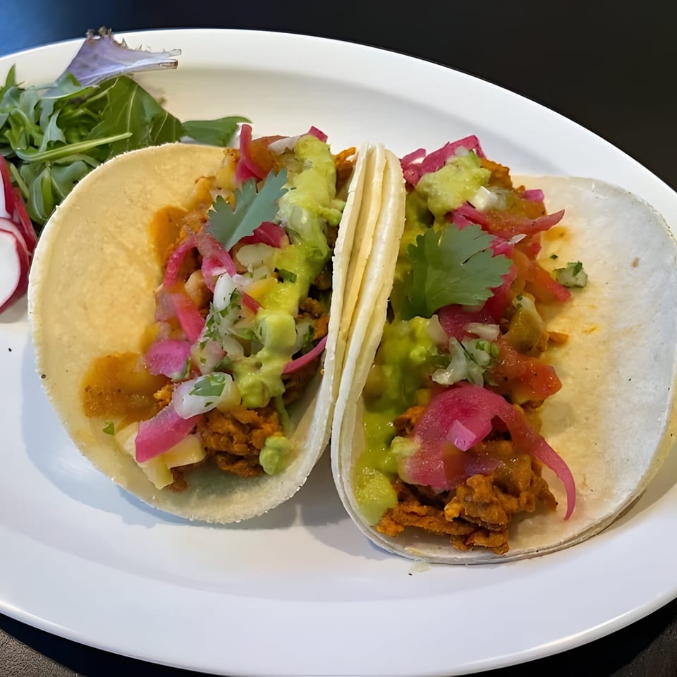 Two Silantro Lime Tacos with meat, guacamole, salsa, and pickled onions on a white plate.