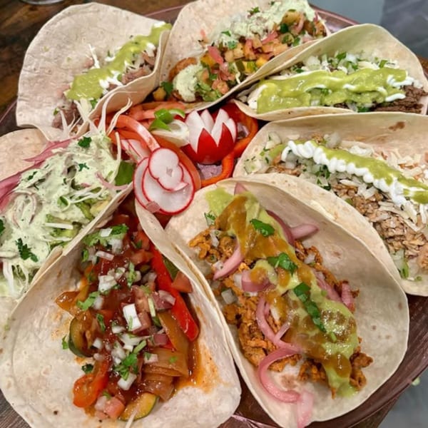 A platter of various Silantro Lime Tacos, garnished with fresh vegetables and sauces.