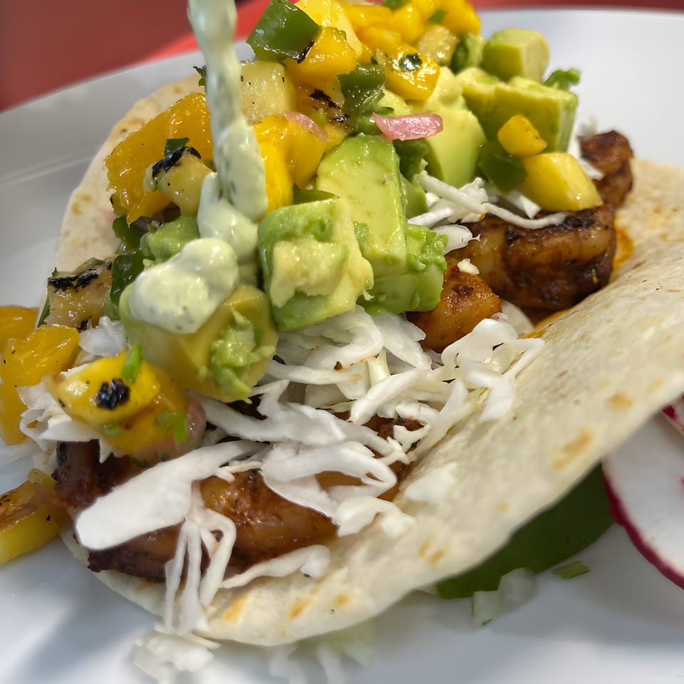 A shrimp taco from Silantro Lime Tacos, topped with mango salsa, avocado, shredded cabbage, and creamy sauce.