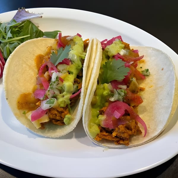 Two Silantro Lime Tacos with meat, guacamole, pickled onions, and cilantro on a white plate.