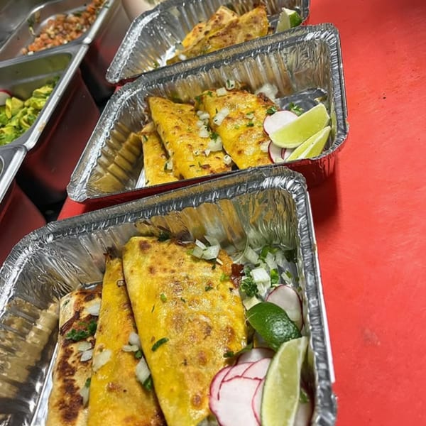 Rows of Silantro Lime Tacos in foil containers, garnished with onions, cilantro, radishes, and lime wedges.